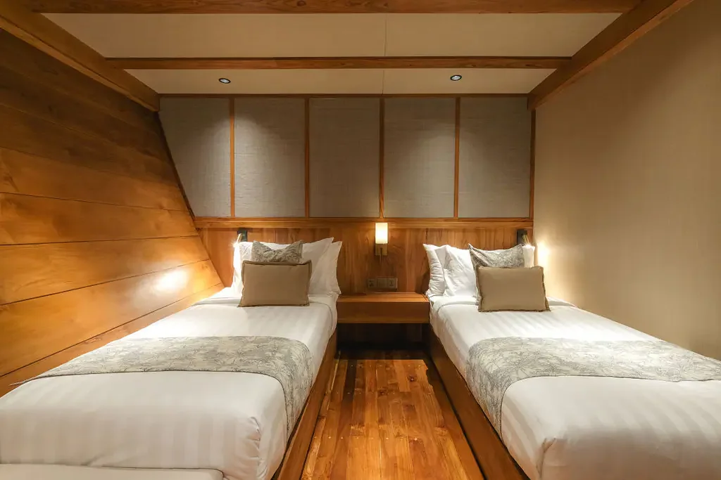 Two separate single beds with a central bedside table in a wood-panelled twin cabin aboard Celestia