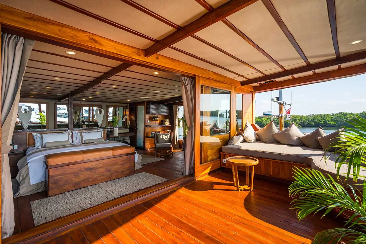 Prana by Atzaró’s Batavia suite with a double bed and wood-panelled interior opening onto a terrace with a cushioned sofa